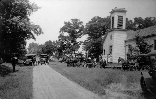 Horses, buggies and early automobiles parked along the road in front of the church in 1919